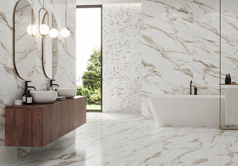 Baño completo con pavimento y revestimiento en azulejo blanco jaspeado. Bañera exenta y mueble suspendido con dos lavabos sobre encimera.