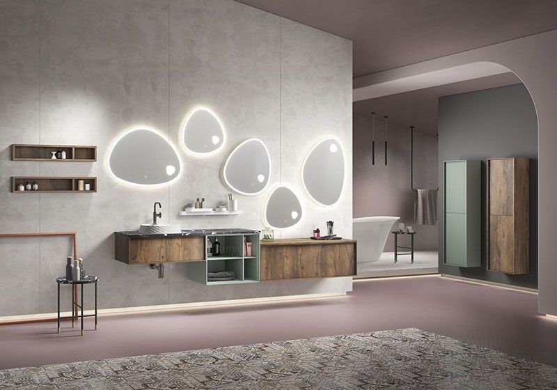 Baño de diseño con mueble de lavabo suspendido y varios espejos con formas, tiene dos armarios suspendidos. Los muebles en tono madera combinado con lacado verde agua.